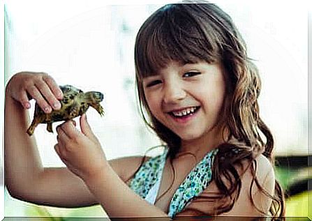 Girl holding a turtle and smiling happily.